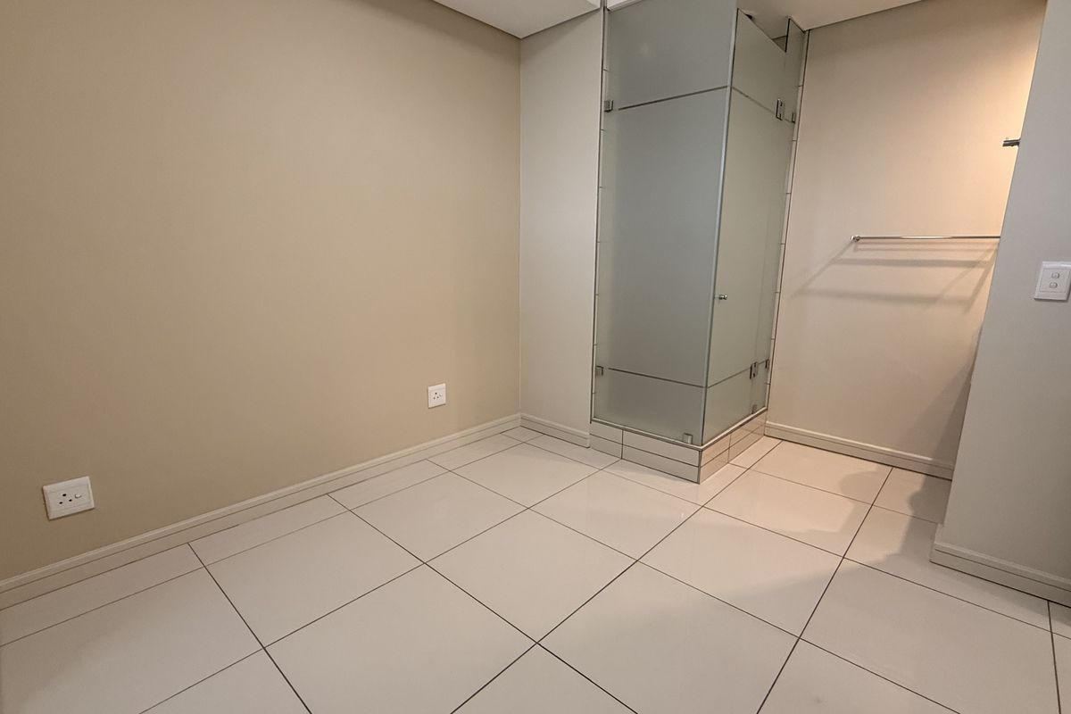 A clean, modern bathroom featuring a glass-enclosed shower, neutral wall tones, and large format floor tiles in an empty, well-maintained space.