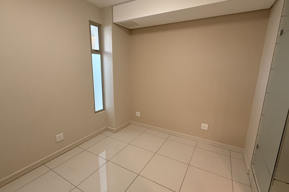A clean, empty bedroom featuring neutral wall tones, tiled flooring, and built-in cupboards, offering a versatile space ready for personalization.