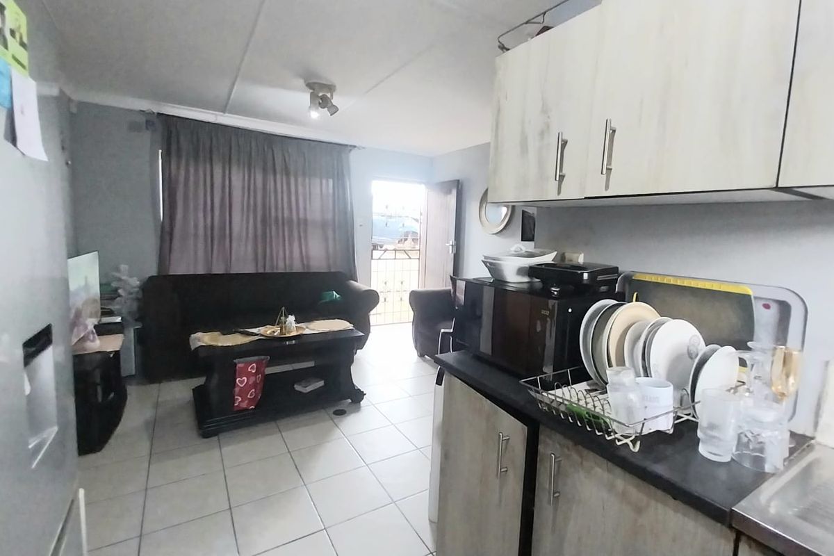 Open-plan living area featuring a compact kitchen with built-in cabinetry and tiled flooring, leading directly to an exterior entrance.