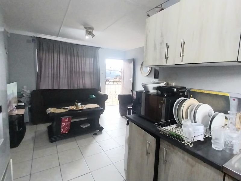 Open-plan living area featuring a compact kitchen with built-in cabinetry and tiled flooring, leading directly to an exterior entrance.