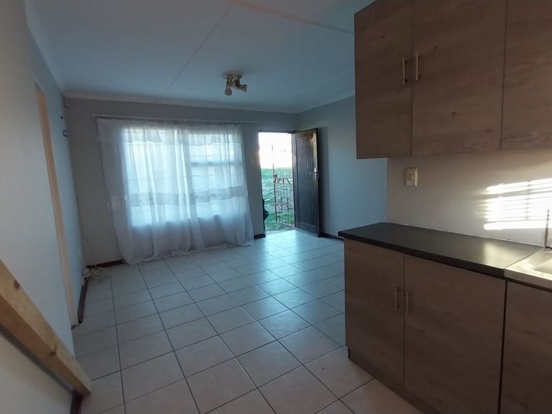 An open-plan living and kitchen area featuring tiled flooring, wood-look cabinetry, and direct access to the exterior.
