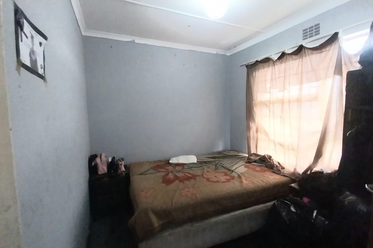 A compact bedroom featuring standard wall finishes, a ceiling cornice, and a ventilation vent, requiring cosmetic updates to improve its overall condition.