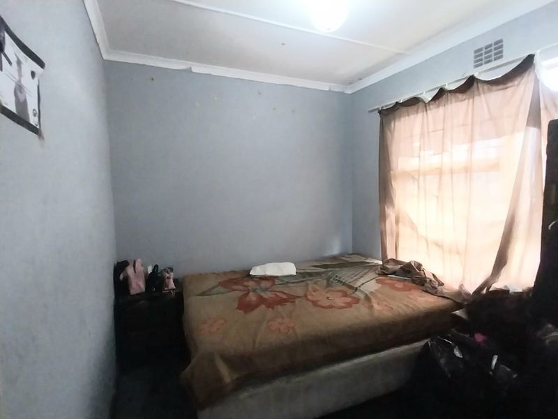 A compact bedroom featuring standard wall finishes, a ceiling cornice, and a ventilation vent, requiring cosmetic updates to improve its overall condition.