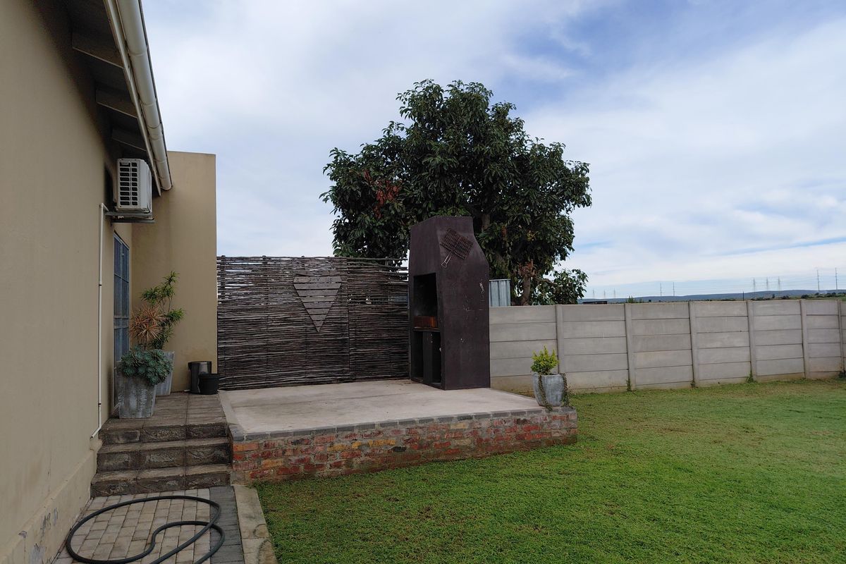 Rear garden area featuring a raised concrete patio with a built-in braai, enclosed by a precast boundary wall and a decorative screen.
