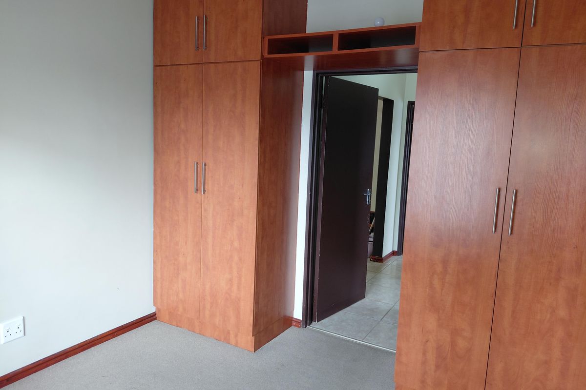A bedroom featuring built-in wooden cupboards with ample storage, neutral carpeting, and a doorway leading to the hallway.