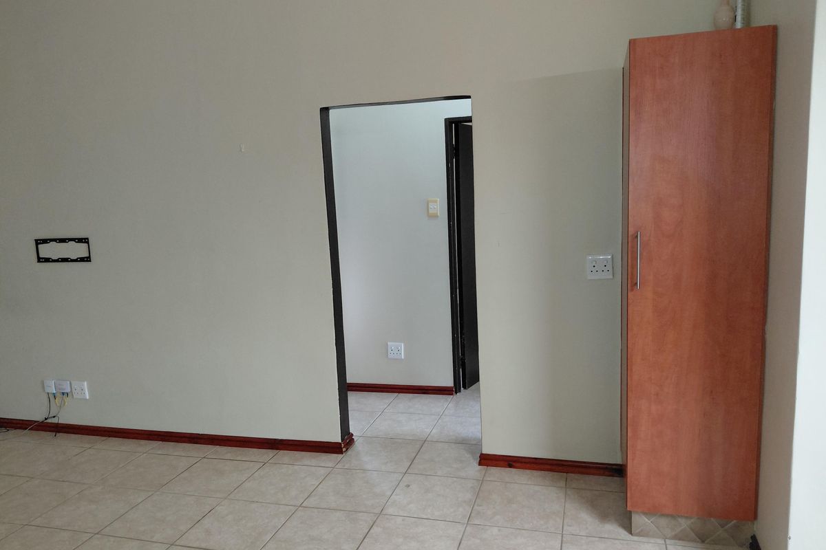 An empty living area featuring tiled flooring, a built-in cupboard, and a doorway leading to an adjacent room.