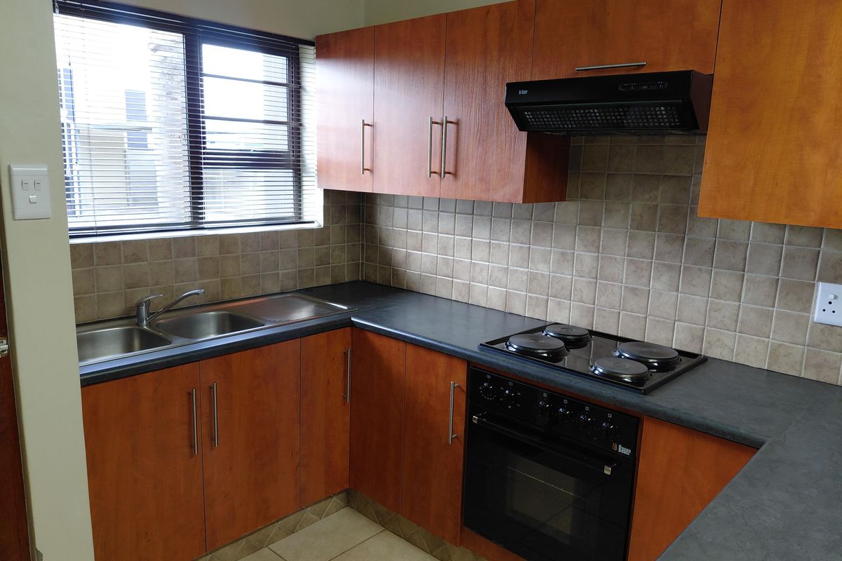 A functional kitchen featuring wood-look laminate cabinetry, dark countertops, a built-in oven with hob, and a tiled backsplash with a double sink.