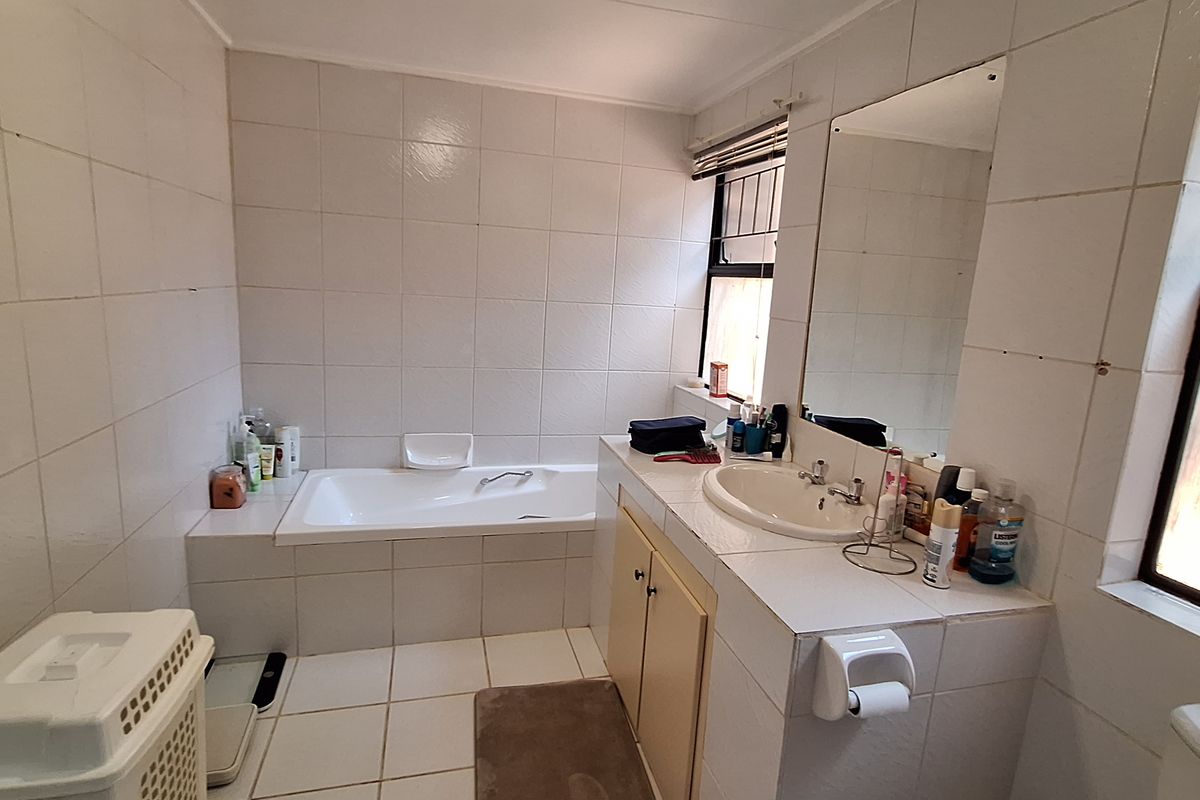A functional bathroom featuring a built-in bathtub, tiled vanity with integrated basin, and wall-mounted mirror, finished with neutral wall and floor tiles.