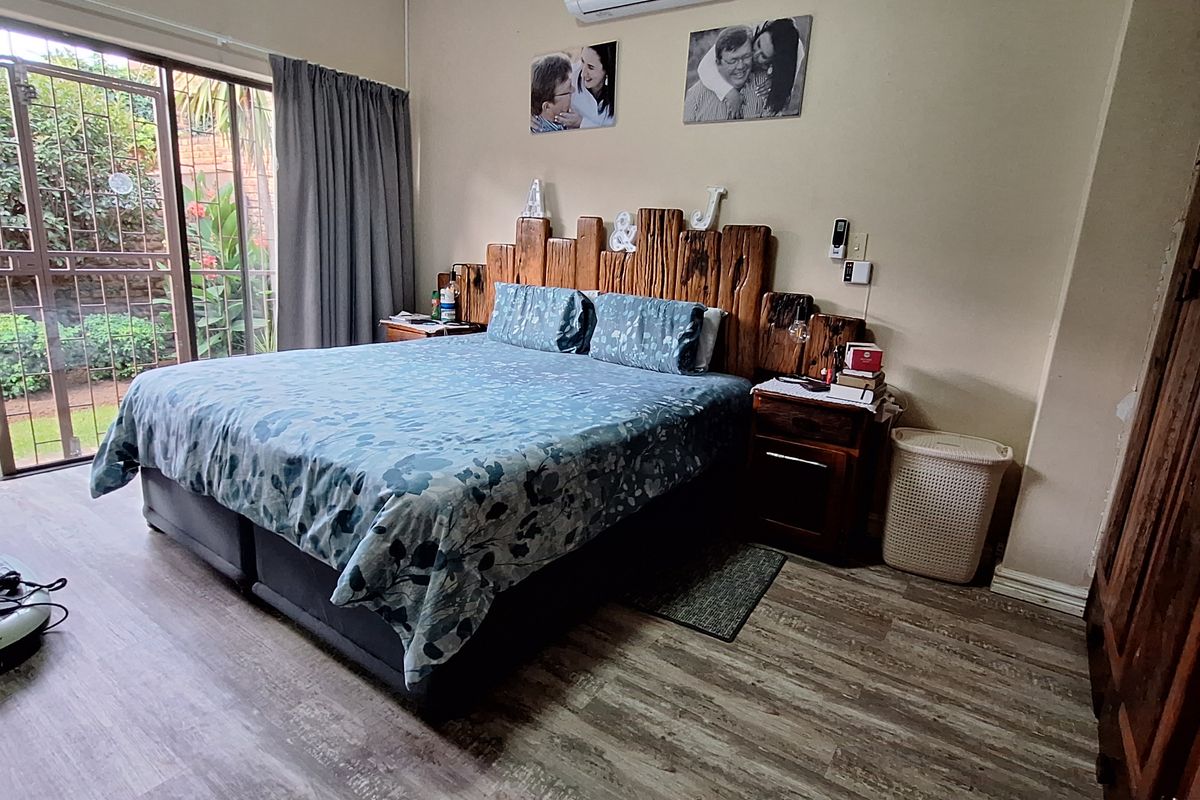 A bedroom featuring wood-look laminate flooring, a wall-mounted air conditioning unit, and sliding glass doors providing direct access to the garden.