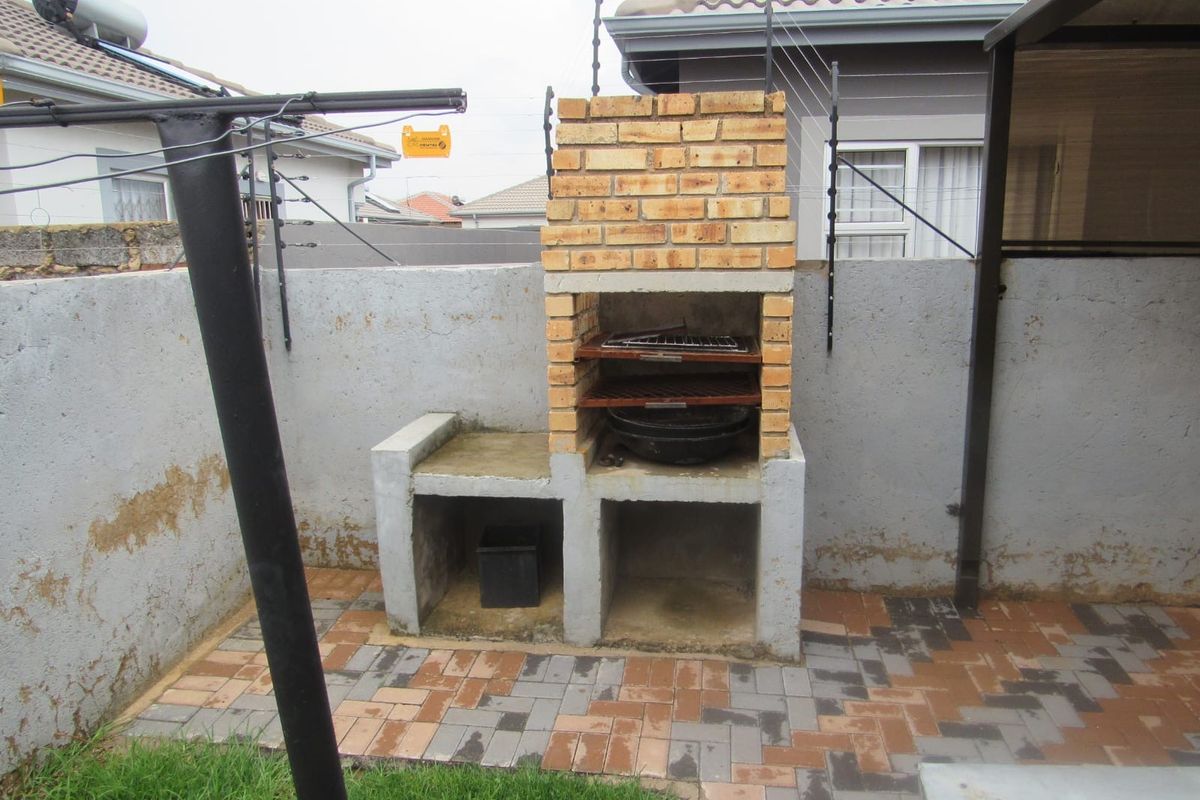 Rear outdoor area featuring a built-in brick braai, paved patio space, and perimeter boundary wall with electric fencing.