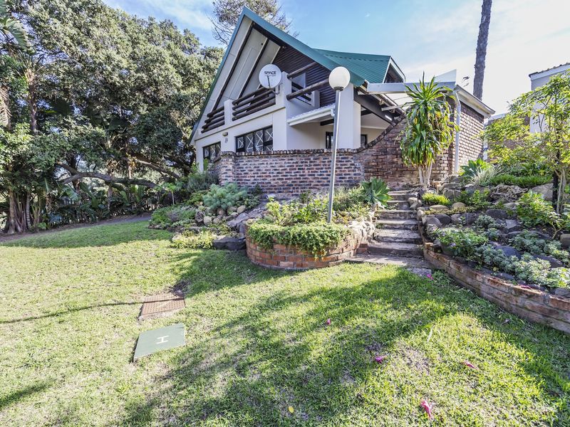 A charming A-frame house featuring a brick retaining wall, landscaped garden, and stone steps leading to the front entrance.