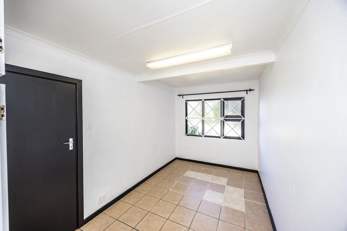 A clean, empty bedroom featuring tiled flooring, a window with security bars, and a simple ceiling light fixture.