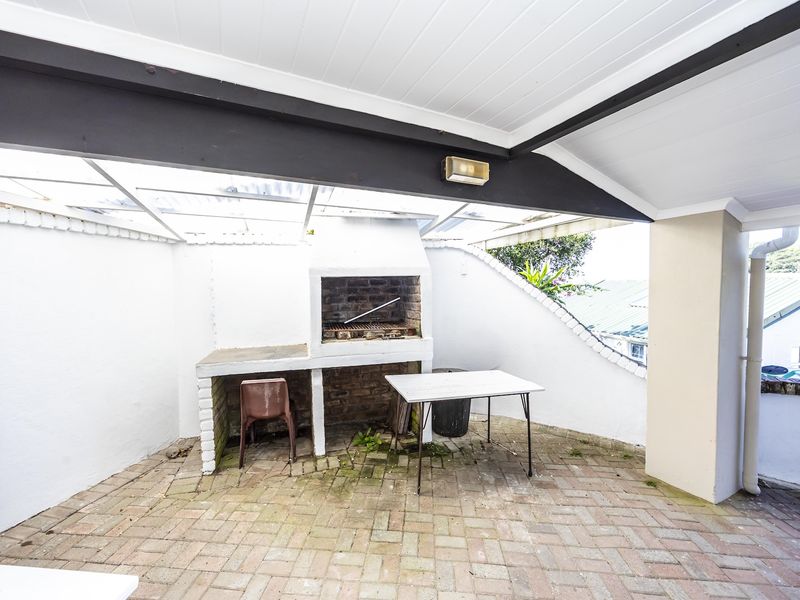 Covered outdoor patio area featuring a built-in brick braai and paved flooring, offering a functional space for outdoor entertaining.