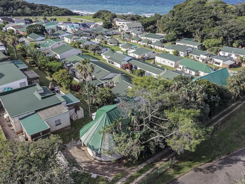 Aerial view of a coastal residential estate featuring multiple units with green metal roofs, surrounded by lush greenery and proximity to the ocean.