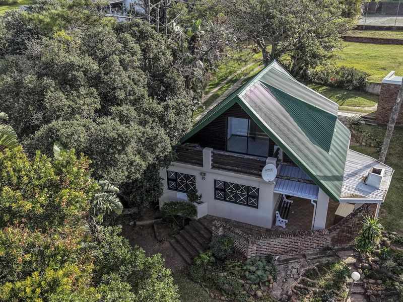 Aerial view of a detached house featuring a pitched metal roof, brick exterior walls, and a balcony, set within a lush, tree-lined garden.