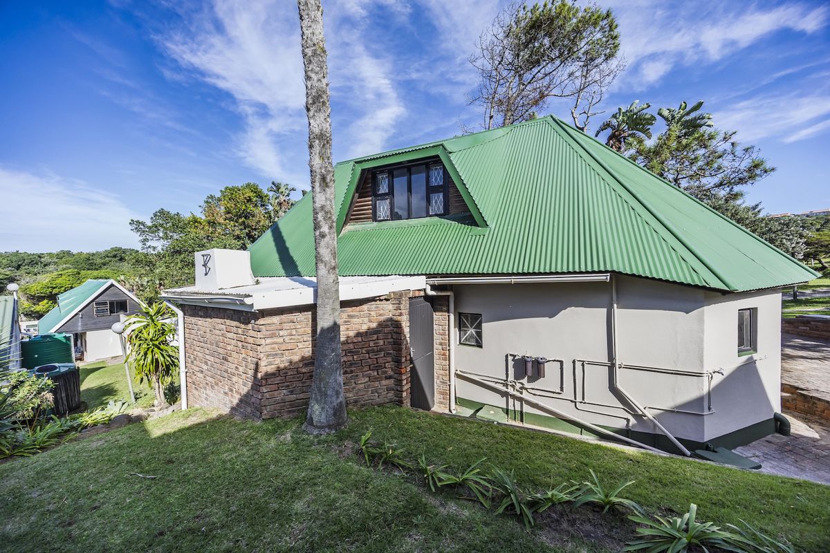 Rear view of a house featuring a green corrugated metal roof, brick and rendered walls, and a dormer window set in a landscaped garden.