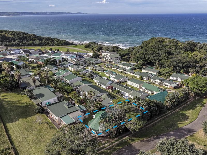 Aerial view of a coastal residential estate featuring multiple homes with pitched roofs, situated near the ocean with surrounding greenery and recreational facilities.