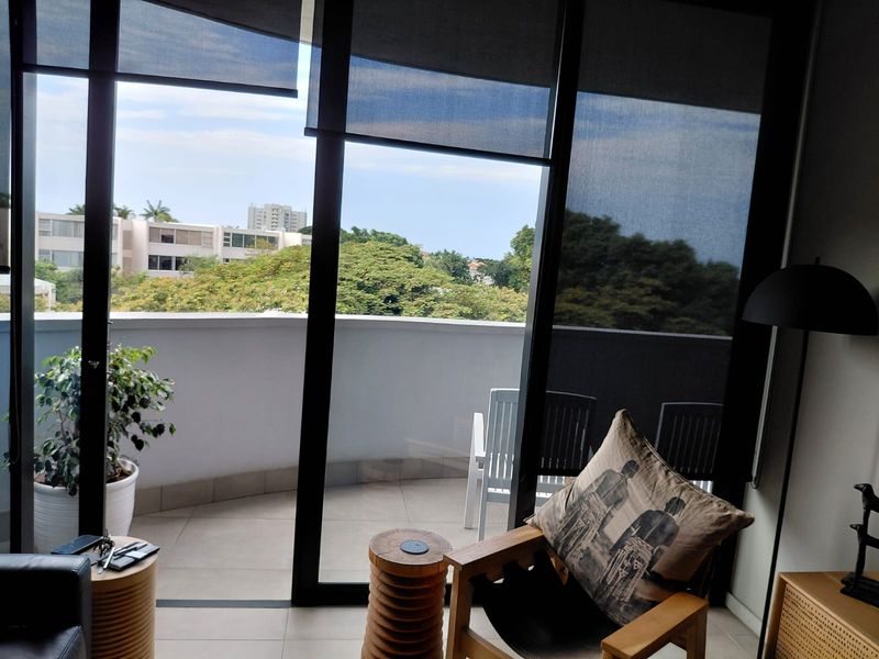 A private balcony featuring tiled flooring and a solid railing, accessible through large sliding glass doors with integrated roller blinds.