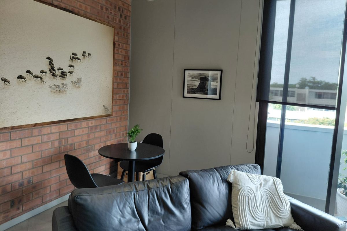 A well-maintained living area featuring an exposed brick feature wall, neutral painted walls, and large glass sliding doors with roller blinds.