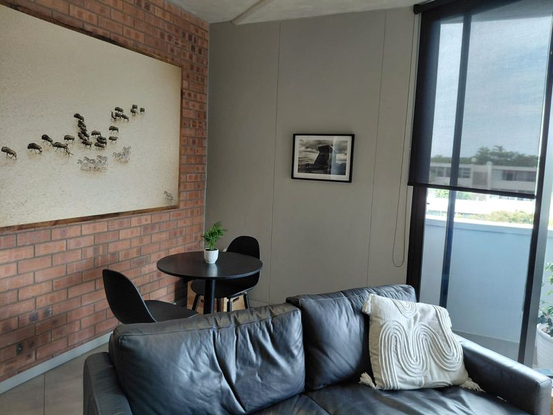 A well-maintained living area featuring an exposed brick feature wall, neutral painted walls, and large glass sliding doors with roller blinds.