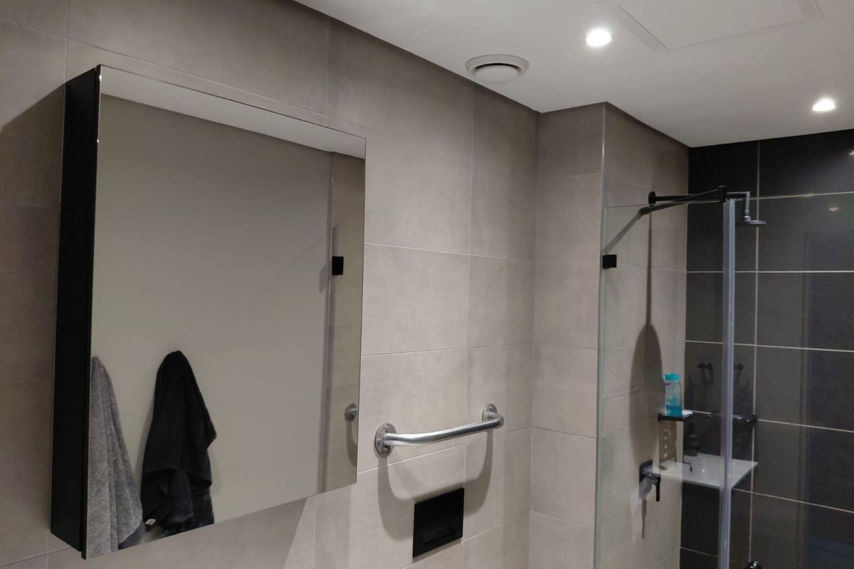 Modern bathroom featuring large format wall tiles, a glass shower enclosure, a wall-mounted mirror cabinet, and a safety grab rail.
