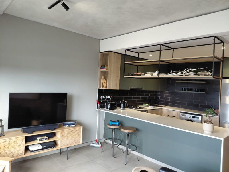 Modern open-plan kitchen and living area featuring sleek cabinetry, stone countertops, black subway tile backsplash, and a stylish suspended metal shelving unit.