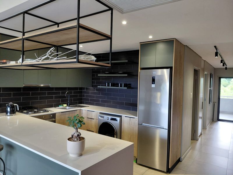 Modern kitchen featuring sleek cabinetry, stone countertops, integrated appliances, and a stylish suspended shelving unit, flowing into a bright hallway.