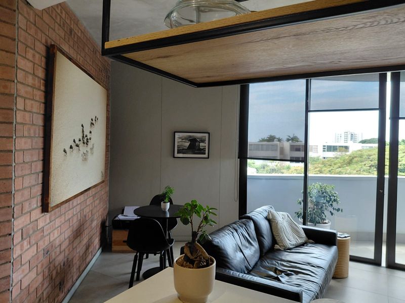 Modern living area featuring an exposed brick feature wall, large floor-to-ceiling glass doors leading to a balcony, and a unique suspended timber shelving unit.