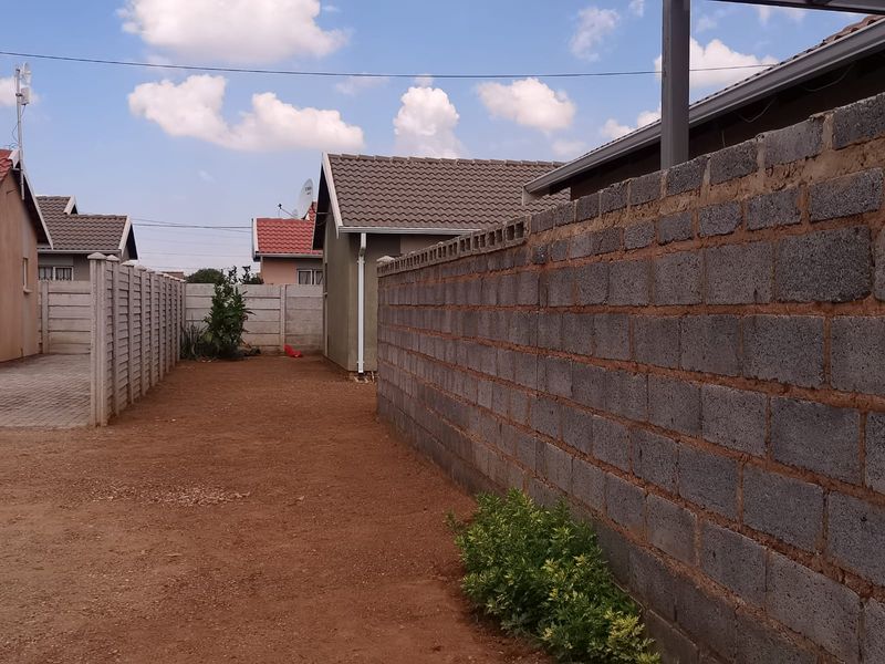 A side yard area featuring a concrete block boundary wall, precast fencing, and an unlandscaped ground surface between neighboring properties.