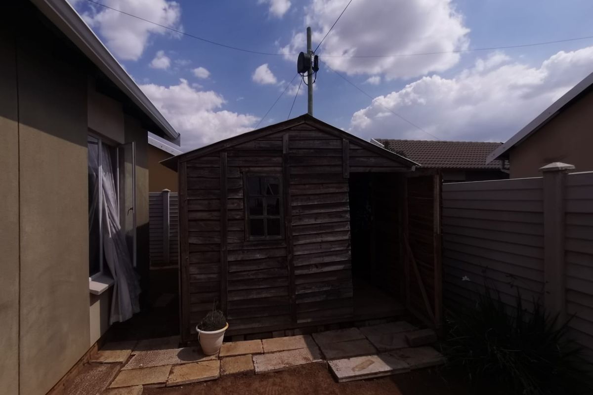 A rear garden area featuring a weathered timber storage shed set on a paved base with surrounding boundary fencing.