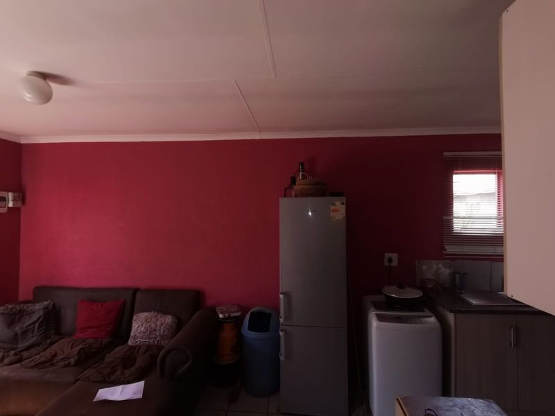 An open-plan living and kitchen area featuring red walls, basic cabinetry, and a sink, requiring cosmetic updates to improve the overall aesthetic.