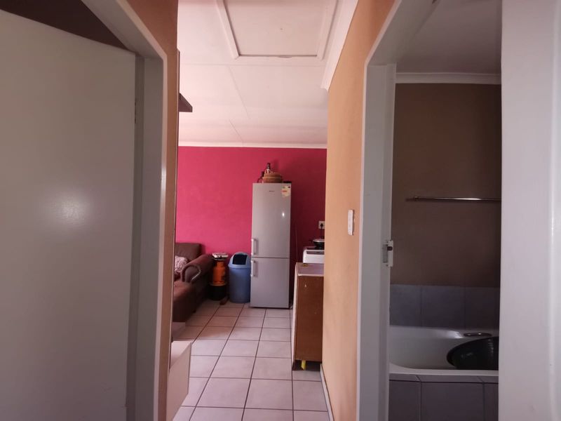 A view from a hallway looking into an open plan living area and a bathroom featuring tiled floors and a built-in bathtub.