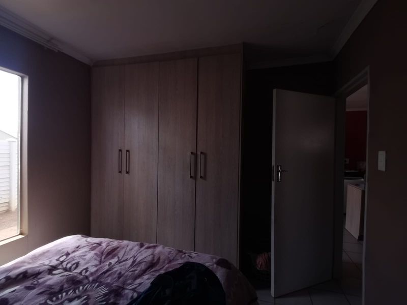 A bedroom featuring built-in wooden cupboards and a window, providing functional storage space within the room.