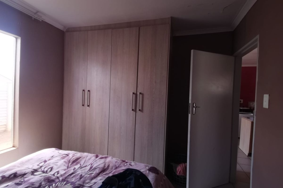 A bedroom featuring built-in wooden cupboards and a ceiling cornice, with a doorway leading to an adjacent room.