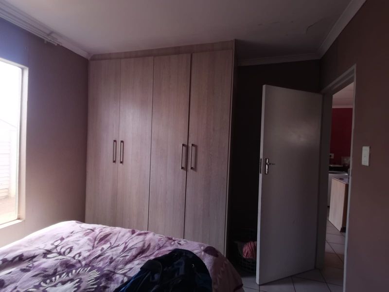 A bedroom featuring built-in wooden cupboards and a ceiling cornice, with a doorway leading to an adjacent room.