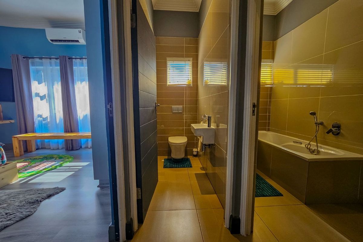 A view from a bedroom into a modern bathroom featuring a separate toilet cubicle and a tiled bathtub area.