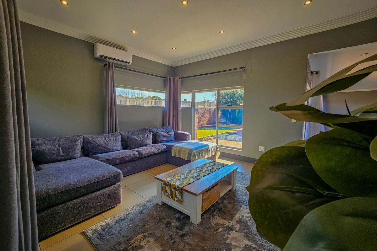 A well-maintained living room featuring tiled flooring, recessed ceiling lighting, and a wall-mounted air conditioning unit, with direct access to the rear garden.