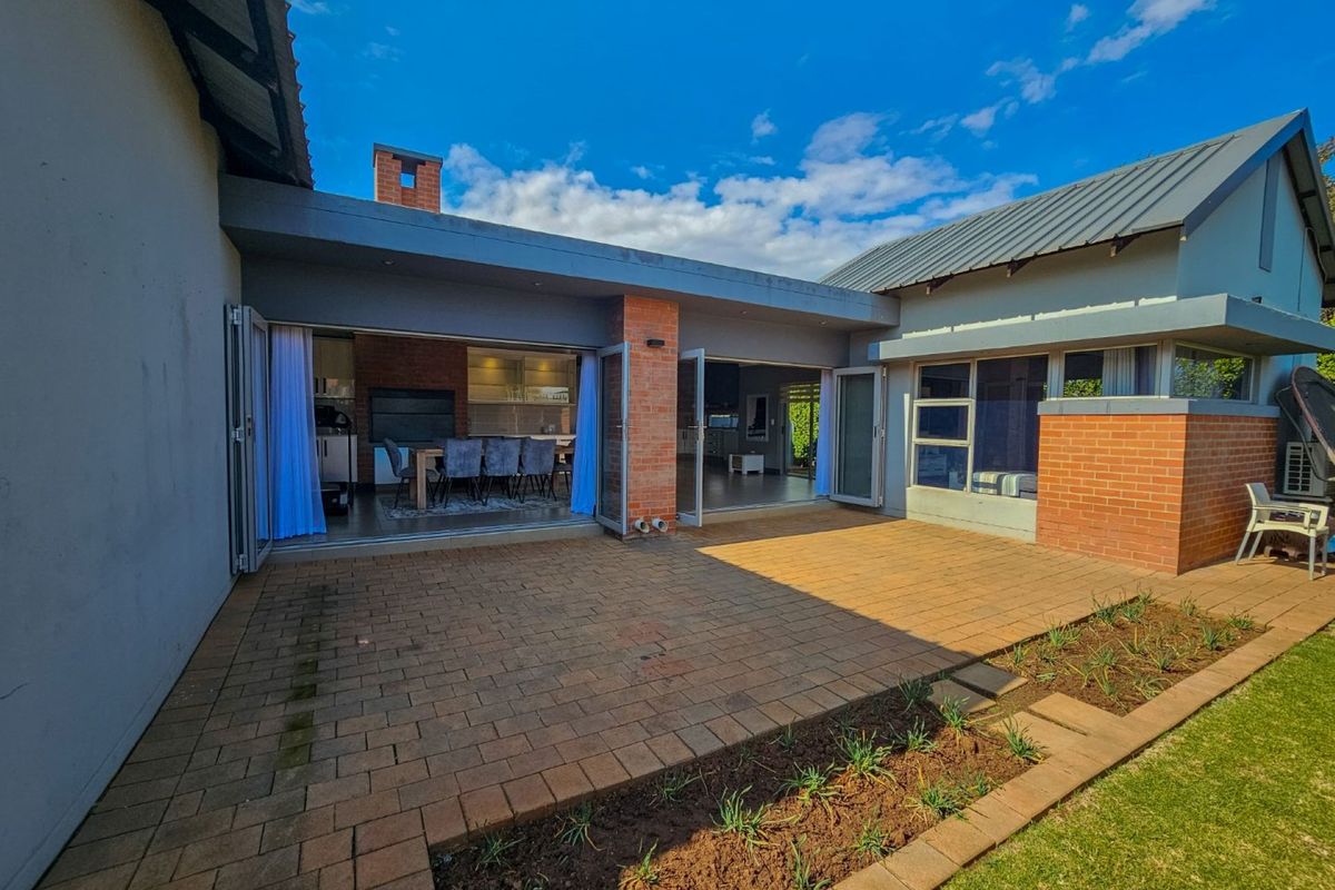 Spacious rear patio featuring brick paving, seamless indoor-outdoor flow through large folding doors, and a built-in brick fireplace, perfect for outdoor entertaining.