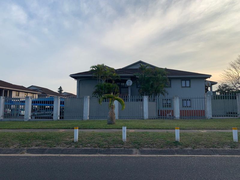 Front elevation of a multi-unit residential flat complex featuring a tiled roof, perimeter fencing, and established landscaping.