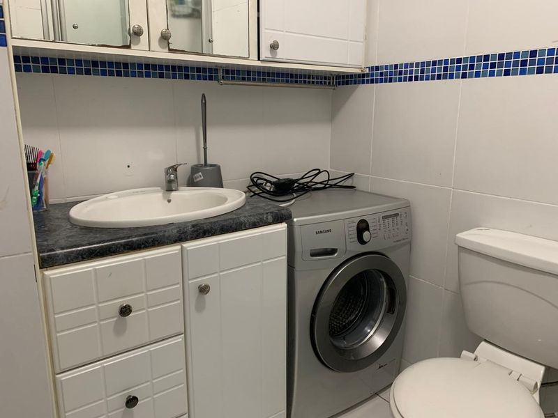 A functional bathroom featuring a vanity cabinet with integrated sink, toilet, and wall tiling, providing essential utility in a compact layout.