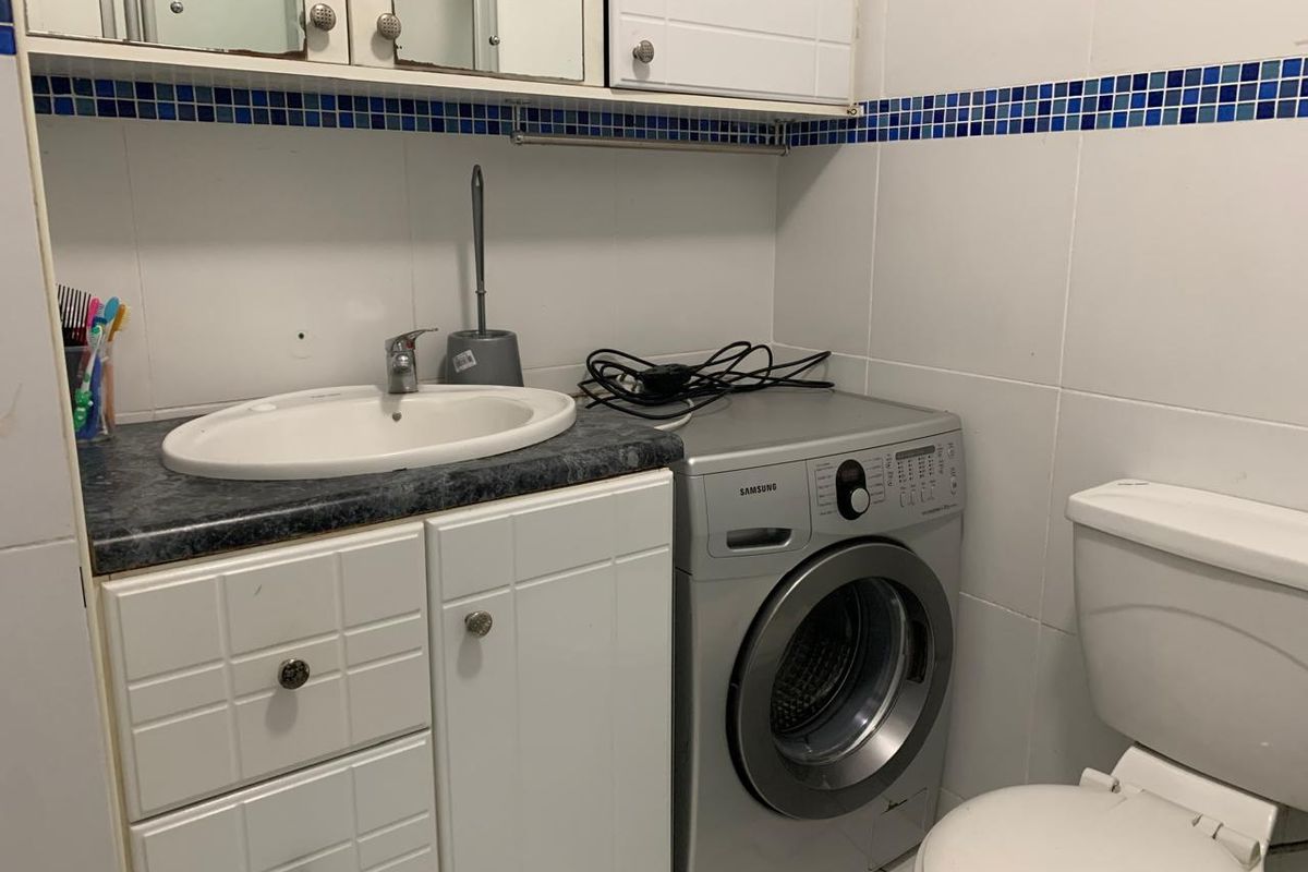 A functional bathroom featuring a vanity cabinet with integrated sink, toilet, and wall tiling, providing essential utility in a compact layout.