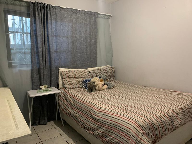 A functional bedroom featuring tiled flooring and a window fitted with security bars.