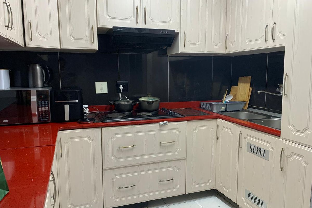 A functional kitchen featuring light-toned cabinetry, a contrasting red stone countertop, black tiled splashback, and integrated hob with extractor fan.