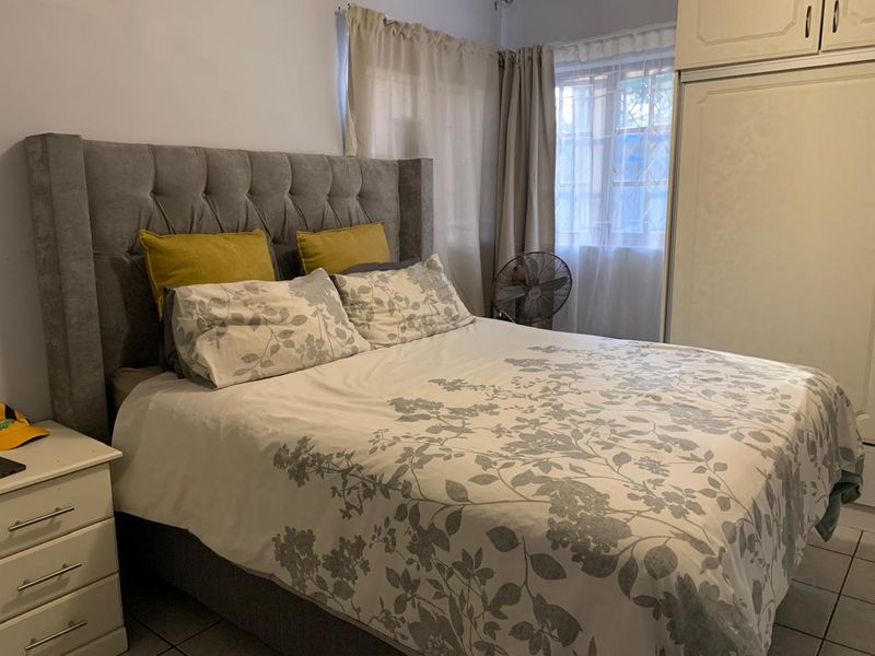 A functional bedroom featuring tiled flooring, a built-in wardrobe, and a window with security bars, providing a practical living space.