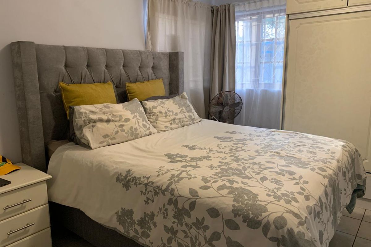A functional bedroom featuring tiled flooring, a built-in wardrobe, and a window with security bars, providing a practical living space.