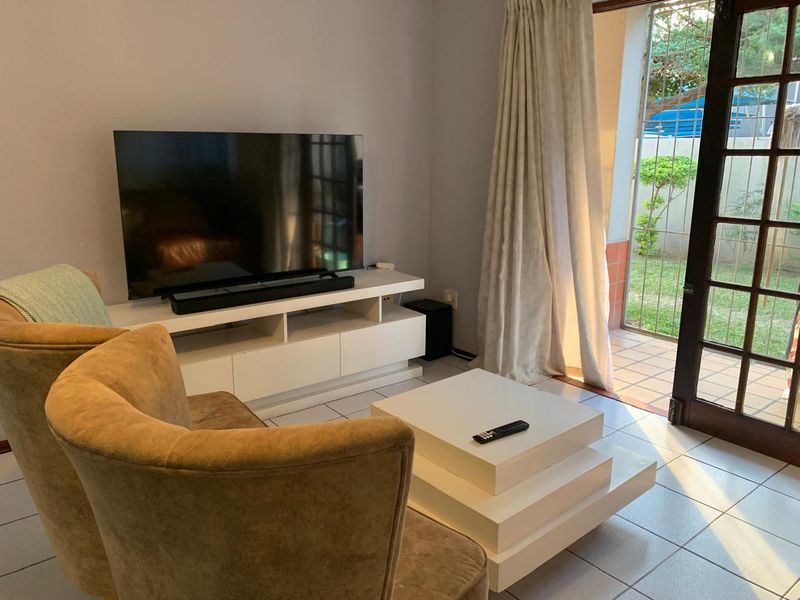 A living room featuring tiled flooring and direct access to an outdoor patio area through glass-paned french doors with security gates.