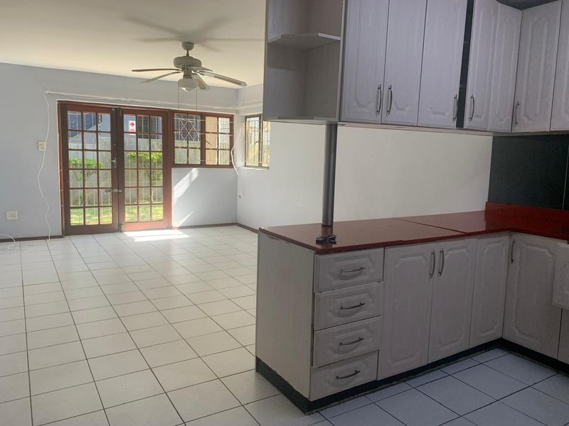 An open-plan living and kitchen area featuring tiled floors, a ceiling fan, and direct access to the garden through glass-paned french doors.