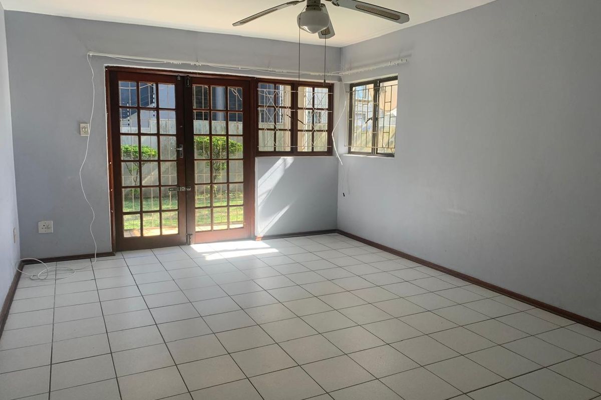 An empty living room featuring tiled flooring, a ceiling fan, and wooden french doors leading to the exterior, secured with metal bars.