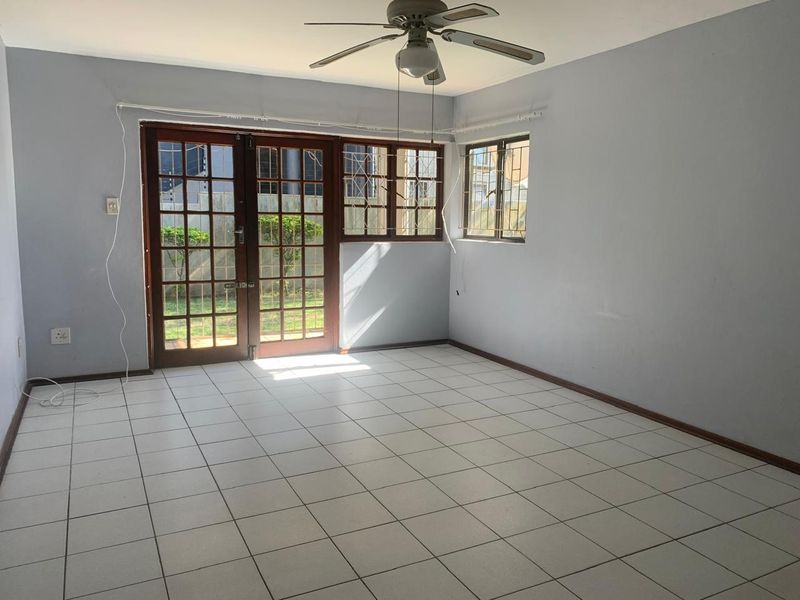 An empty living room featuring tiled flooring, a ceiling fan, and wooden french doors leading to the exterior, secured with metal bars.