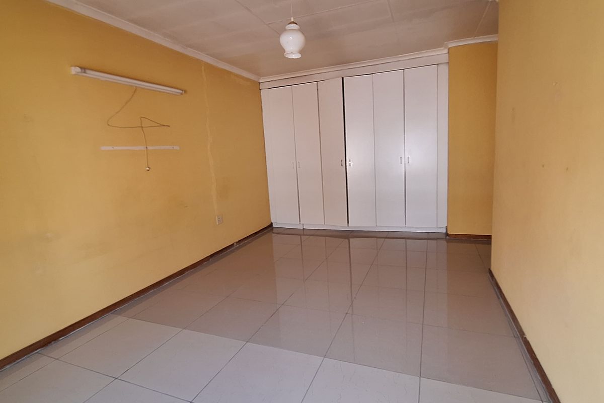 An empty bedroom featuring tiled flooring, built-in white wardrobes, and yellow painted walls, offering a blank canvas for renovation or restyling.